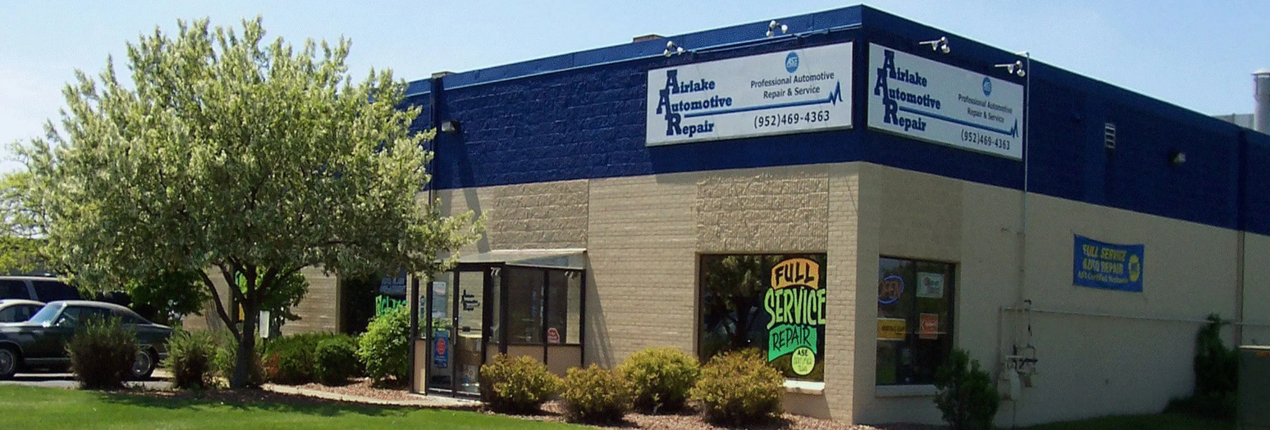 Auto repair shop exterior with signage and trees.